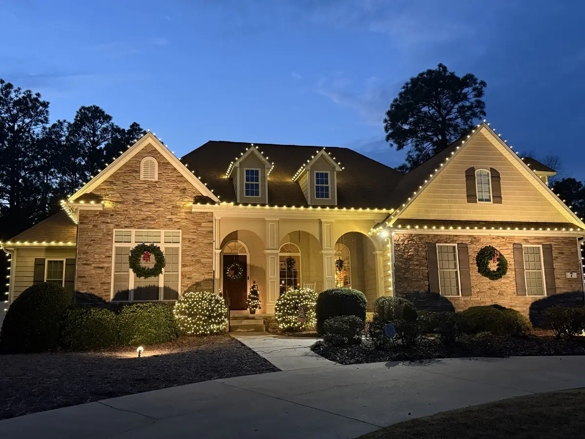 A Sandhills home lit by PineLights, with warm white lights along every roofline and lit shrubs by the front porch